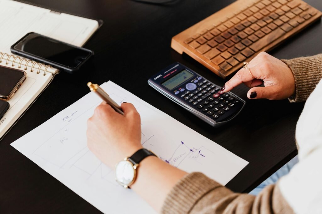 pexels-photo-4476375-4476375-1 Close-up of hands working with a calculator and notebook on a desk, analyzing documents.
